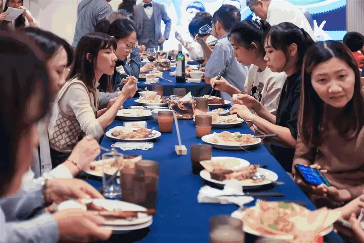 小型婚宴長桌併成一整排，賓客用餐，盡頭是投影幕