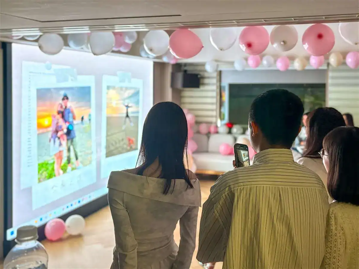 賓客站在投影幕前看新人照片，天花板掛著粉白氣球