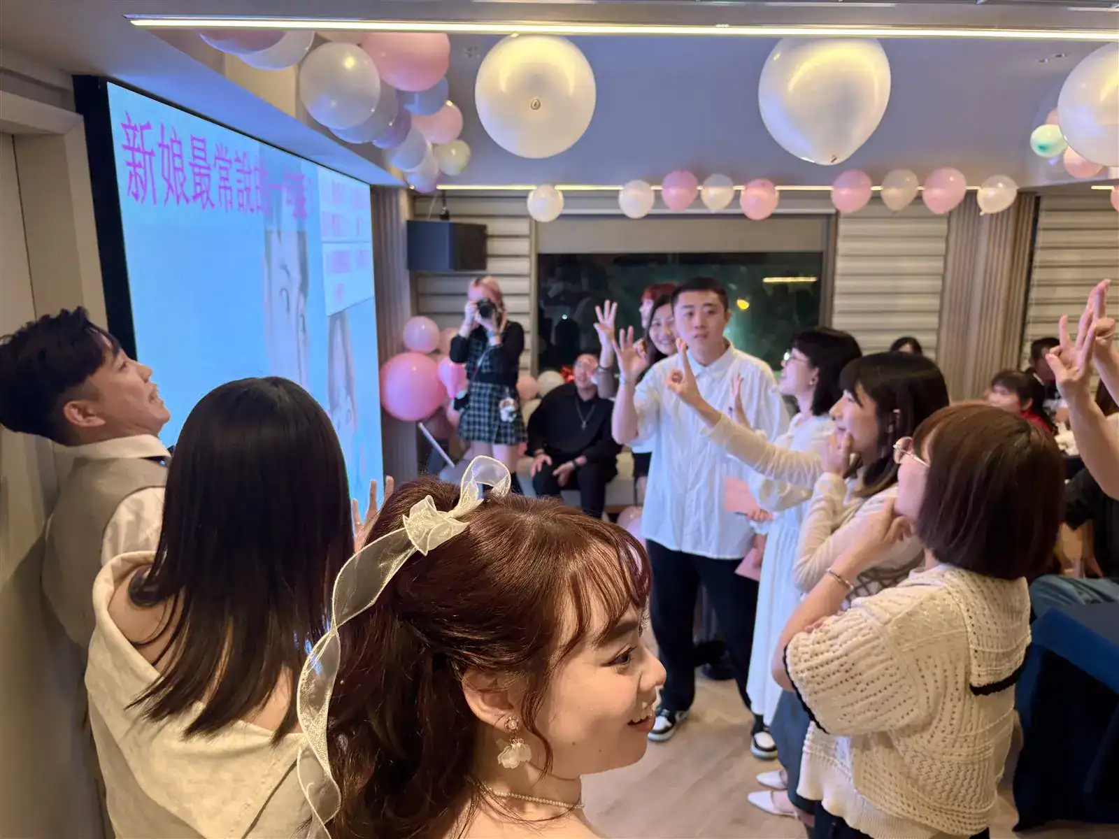 台中婚禮派對後半場，新人和賓客在投影幕前玩新娘問答遊戲，天花板掛滿粉白氣球